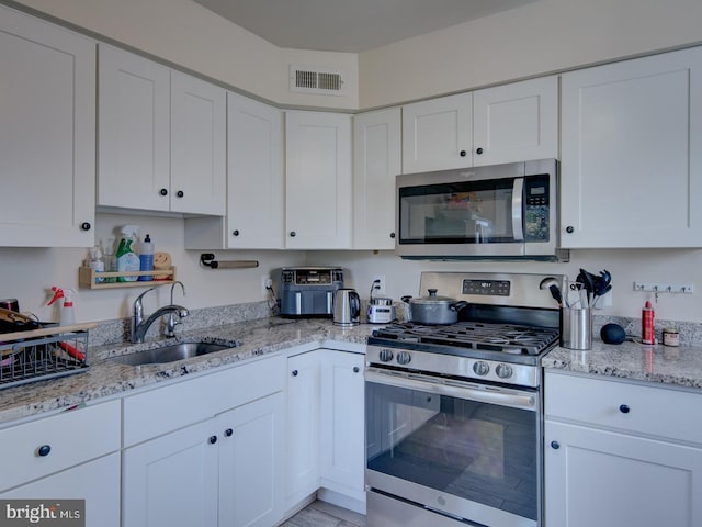 kitchen featuring white cabinets, stainless steel appliances, light stone countertops, and sink