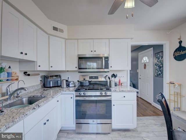 kitchen featuring ceiling fan, sink, light stone countertops, white cabinets, and appliances with stainless steel finishes