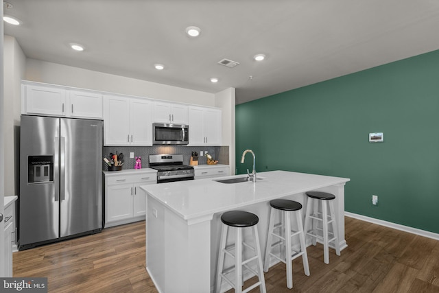 kitchen featuring decorative backsplash, appliances with stainless steel finishes, sink, a center island with sink, and white cabinets