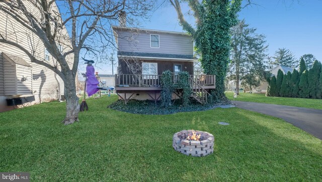 rear view of property with a deck, an outdoor fire pit, and a lawn