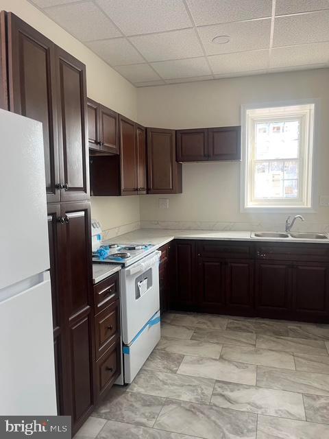 kitchen with sink, white appliances, dark brown cabinetry, and a drop ceiling