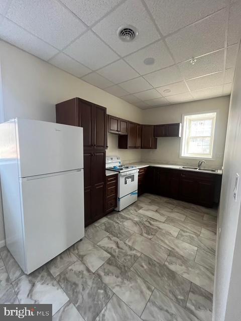 kitchen with sink, white appliances, dark brown cabinets, and a drop ceiling