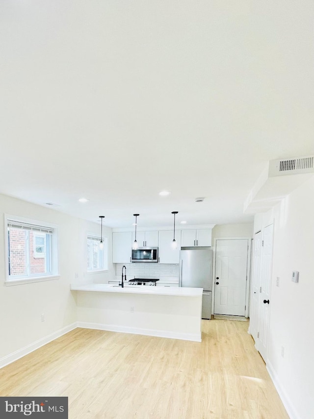 kitchen with light wood-type flooring, backsplash, stainless steel appliances, white cabinets, and hanging light fixtures