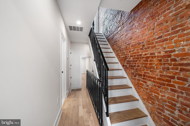 stairway with brick wall and wood-type flooring