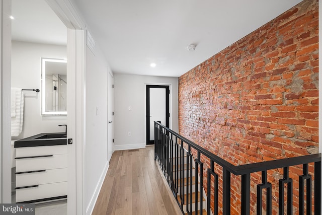 hallway with sink, light wood-type flooring, and brick wall