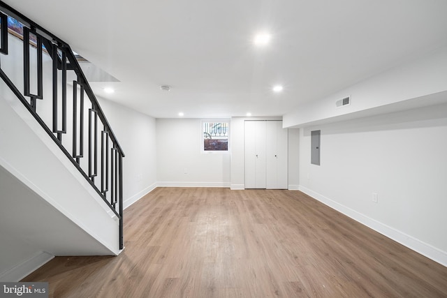 basement featuring electric panel and light hardwood / wood-style floors