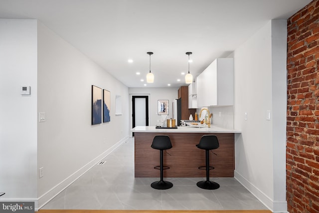 kitchen with kitchen peninsula, pendant lighting, a breakfast bar, white cabinetry, and sink