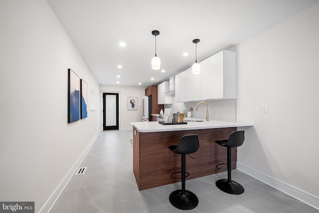 kitchen featuring decorative light fixtures, white cabinets, a kitchen bar, refrigerator, and kitchen peninsula