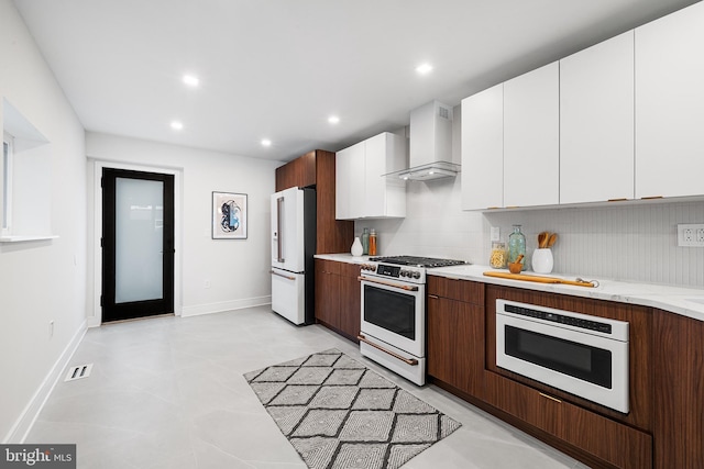 kitchen featuring white appliances, wall chimney exhaust hood, tasteful backsplash, and white cabinetry