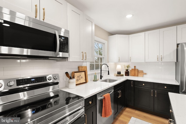 kitchen featuring white cabinets, dark cabinetry, stainless steel appliances, and a sink