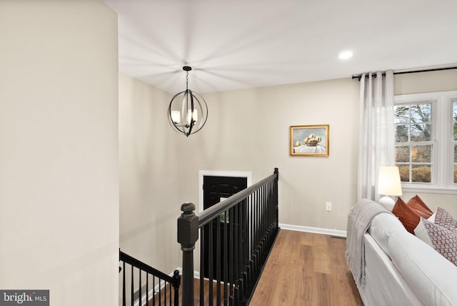 hallway with baseboards, a chandelier, wood finished floors, and an upstairs landing