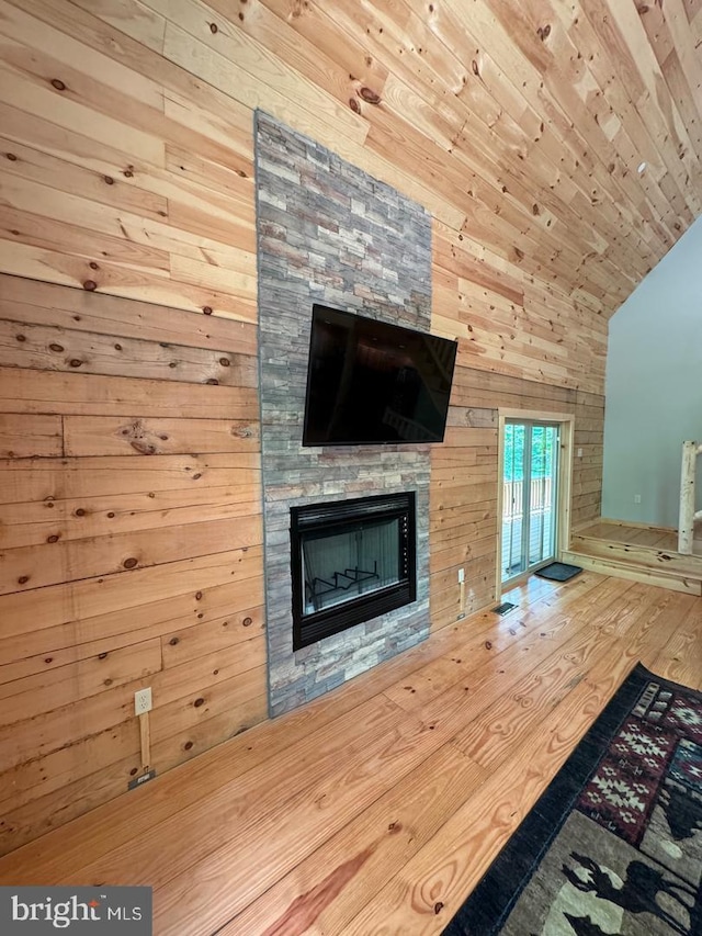 unfurnished living room with hardwood / wood-style flooring, wood walls, a stone fireplace, and lofted ceiling