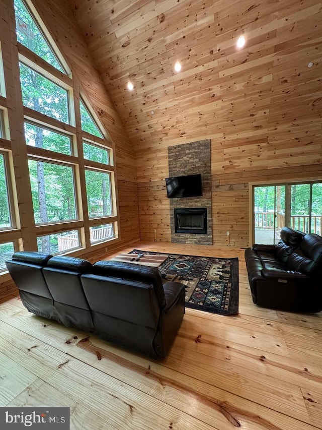 living room with high vaulted ceiling, hardwood / wood-style flooring, a stone fireplace, and wooden walls