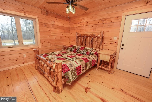 bedroom with ceiling fan, light hardwood / wood-style floors, wooden ceiling, and wooden walls