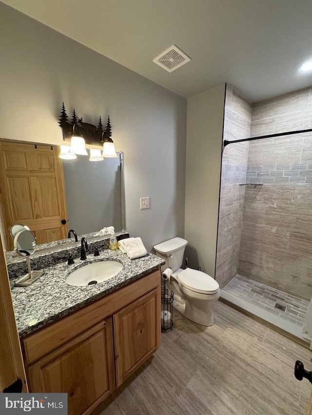 bathroom with hardwood / wood-style flooring, vanity, toilet, and tiled shower