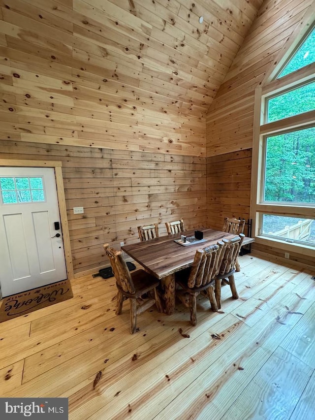 dining room with wood walls, high vaulted ceiling, and light wood-type flooring