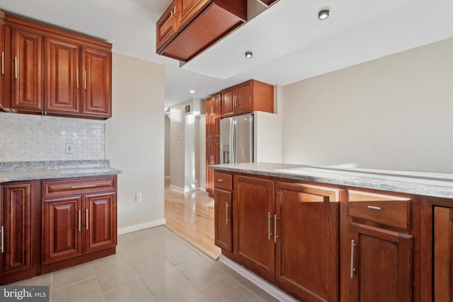 kitchen with light stone counters, stainless steel fridge with ice dispenser, backsplash, and light tile patterned floors