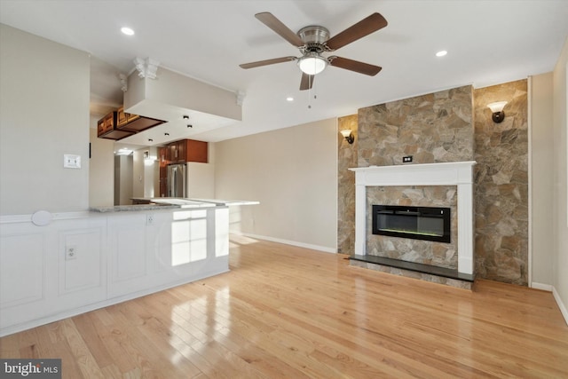 unfurnished living room featuring ceiling fan, a stone fireplace, and light wood-type flooring