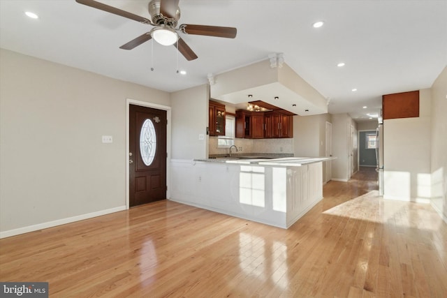 kitchen featuring kitchen peninsula, decorative backsplash, ceiling fan, sink, and light hardwood / wood-style flooring