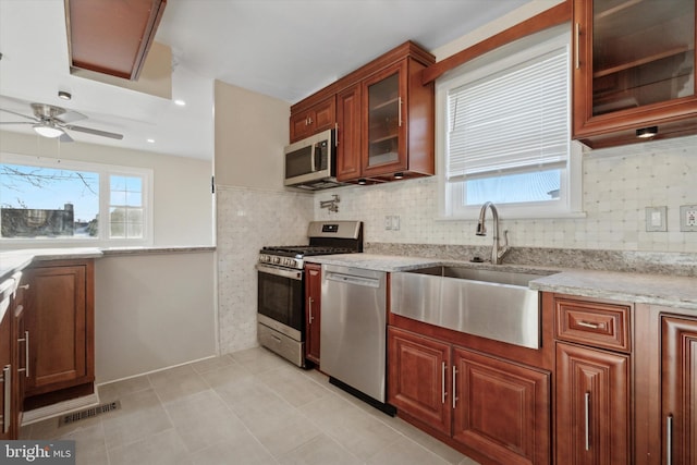 kitchen featuring backsplash, sink, ceiling fan, light stone countertops, and appliances with stainless steel finishes