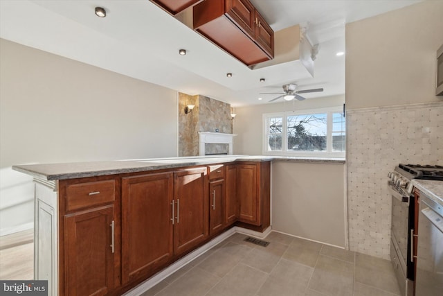 kitchen featuring gas stove, kitchen peninsula, ceiling fan, and light tile patterned floors