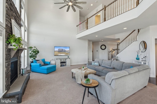 carpeted living room with a high ceiling, a stone fireplace, and ceiling fan