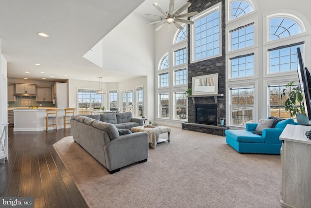 living room with hardwood / wood-style floors, a towering ceiling, a stone fireplace, and ceiling fan