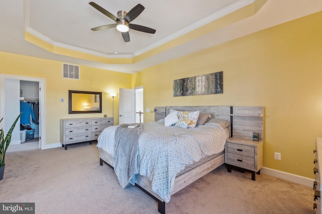 bedroom with crown molding, ceiling fan, a tray ceiling, light carpet, and a closet