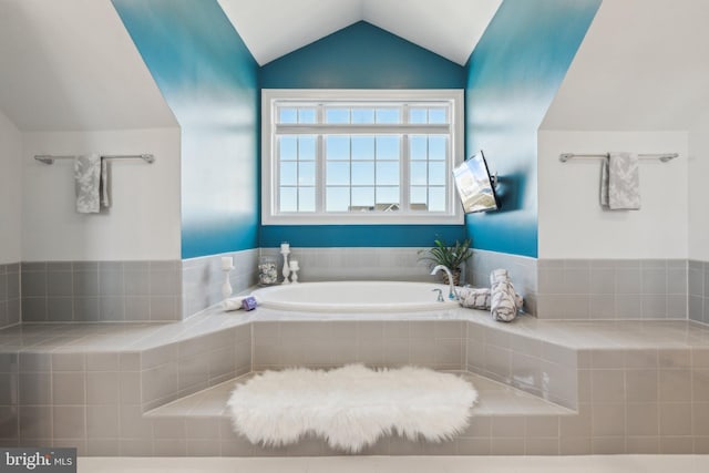 bathroom featuring a relaxing tiled tub and lofted ceiling