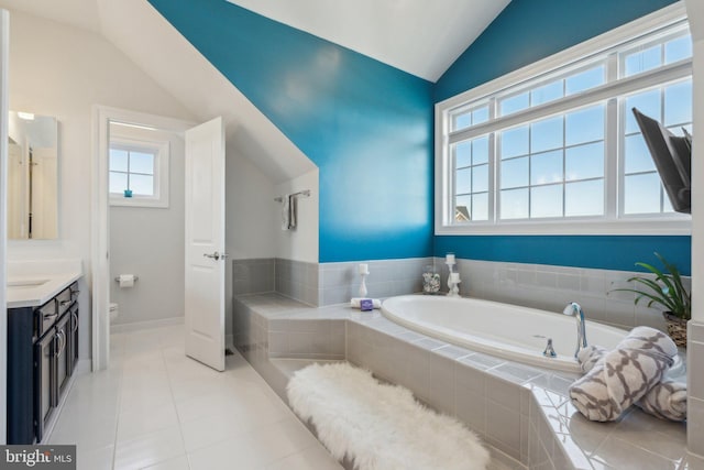 bathroom with lofted ceiling, toilet, vanity, tiled bath, and tile patterned flooring