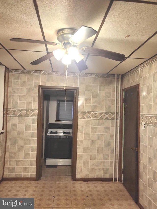 kitchen with white gas range, ceiling fan, and tile walls