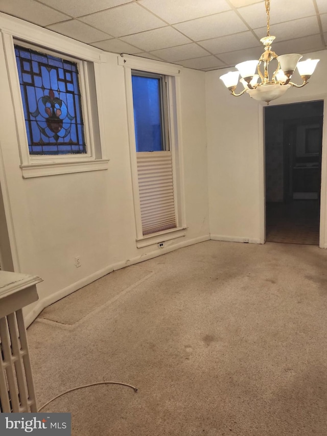 carpeted empty room with a paneled ceiling and a notable chandelier