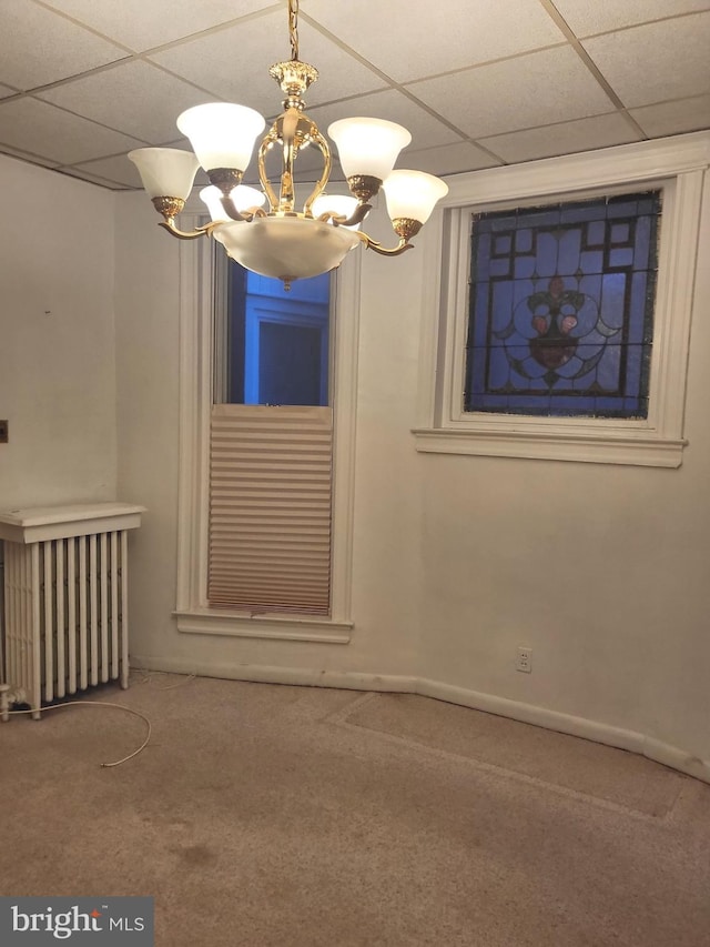 empty room with a chandelier, radiator heating unit, carpet floors, and a drop ceiling