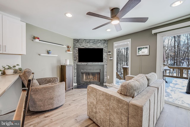 living room featuring ceiling fan, light hardwood / wood-style floors, and a stone fireplace