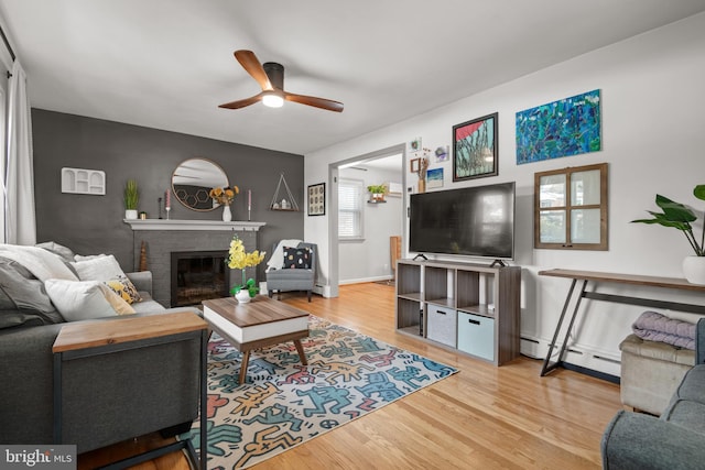 living room featuring a brick fireplace, ceiling fan, a baseboard radiator, and hardwood / wood-style flooring