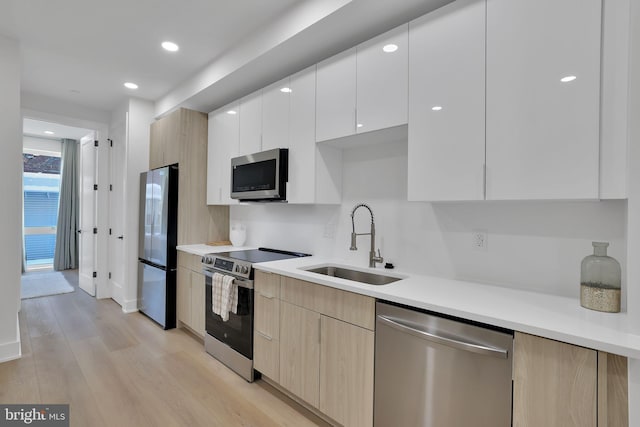 kitchen with appliances with stainless steel finishes, light brown cabinetry, sink, white cabinets, and light wood-type flooring