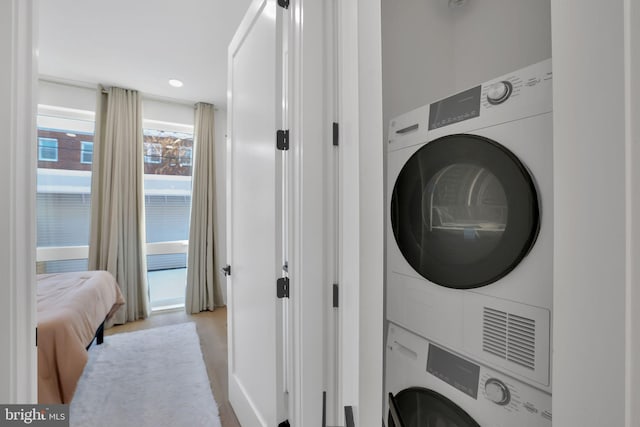 laundry area with stacked washer and dryer and light hardwood / wood-style flooring