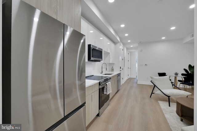 kitchen featuring appliances with stainless steel finishes, light brown cabinetry, sink, white cabinets, and light wood-type flooring