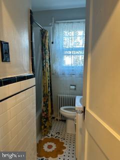 bathroom featuring radiator, shower / bath combo, tile patterned floors, toilet, and tile walls