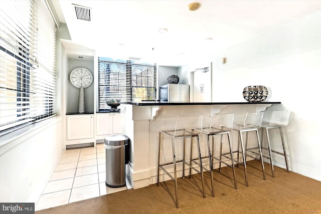 kitchen with a breakfast bar, white cabinets, light tile patterned flooring, kitchen peninsula, and stainless steel refrigerator