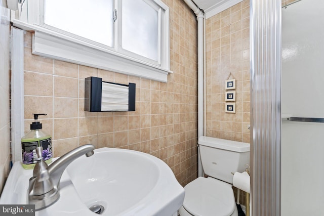 bathroom featuring toilet, sink, a wealth of natural light, and tile walls