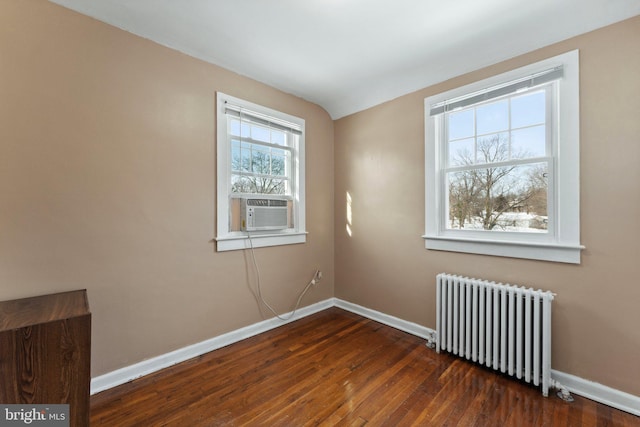 spare room featuring cooling unit, dark wood-type flooring, radiator, and vaulted ceiling