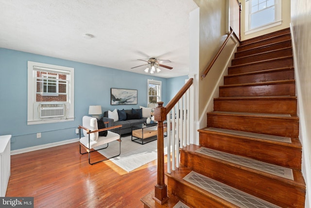 stairway with ceiling fan, cooling unit, wood-type flooring, and a wealth of natural light