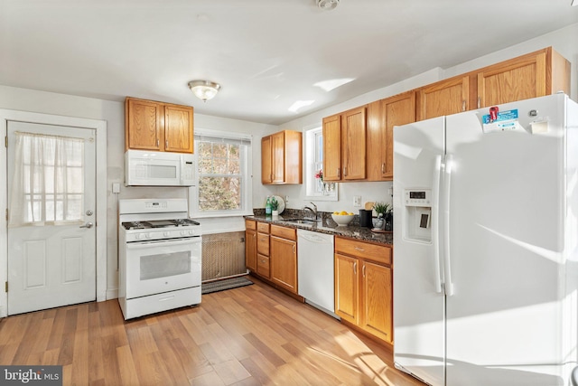 kitchen with light wood-type flooring, white appliances, and dark stone counters