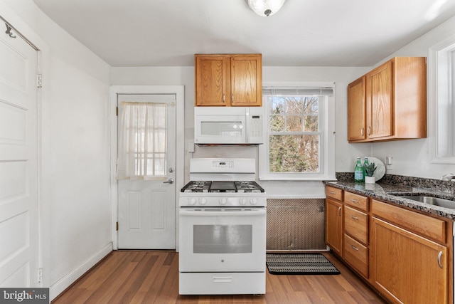 kitchen with dark stone countertops, sink, light hardwood / wood-style floors, and white appliances