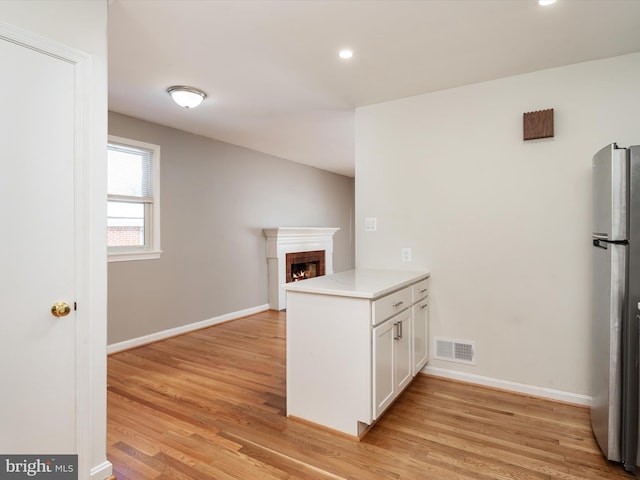 kitchen with kitchen peninsula, white cabinetry, stainless steel refrigerator, and light hardwood / wood-style flooring