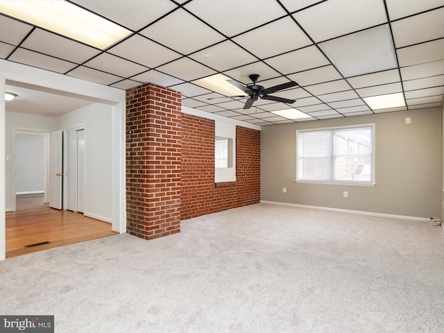 unfurnished living room featuring a paneled ceiling, ceiling fan, light colored carpet, and brick wall