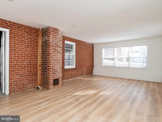 unfurnished living room featuring light wood-type flooring and brick wall