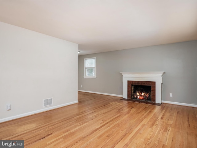 unfurnished living room with light hardwood / wood-style floors and a brick fireplace