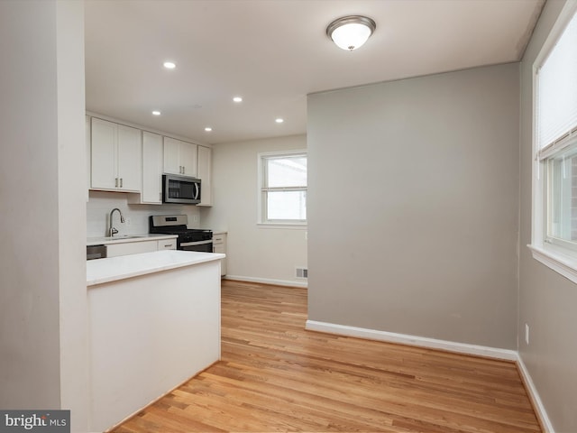 kitchen featuring white cabinets, sink, light hardwood / wood-style flooring, decorative backsplash, and appliances with stainless steel finishes